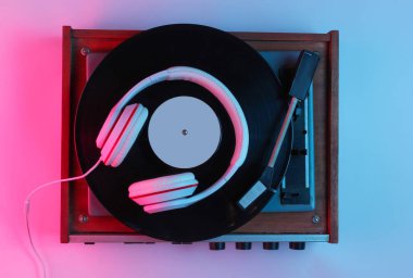 Retro tarzı müzik konsepti. Klasik kulaklıklar, gradyan pembe neon ışıklı vinil plak çalar. Popüler kültür. 80 'ler. Üst görünüm