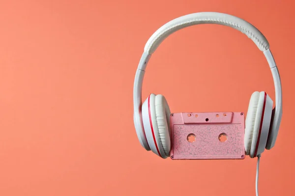 White classic wired headphones with audio cassette isolated on coral color background. Retro style. 80s. Minimalistic music concept.