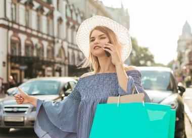 Genç ve çekici bir kadın, bir araba yakalamak ve şehrin yol kenarında telefonla konuşmak için el kol hareketi yapıyor. Otostop konsepti