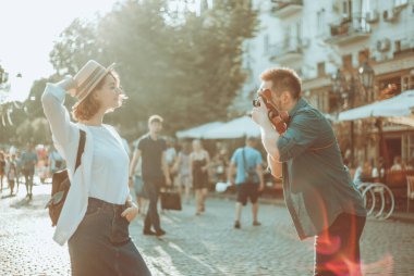 Genç, neşeli bir çift hippi şehirde yürürken retro kamerayla çekiliyor. Erkek fotoğrafçı şık giyinmiş genç bir kadının fotoğraflarını çekiyor.