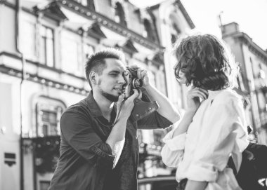 Genç, neşeli bir çift hippi şehirde yürürken retro kamerayla çekiliyor. Erkek fotoğrafçı şık giyinmiş genç bir kadının fotoğraflarını çekiyor.