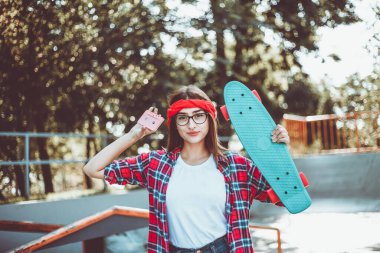 Geçmişe dönük gençlik bakışı. 80 'ler. Parlak güneşli bir günde kaykay parkında kameraya poz verirken kaykay ve ses kaseti tutan şık giyimli çekici bir hippi kadın.