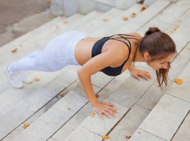 Genç sporcu kadın egzersizle vücudunu değiştiriyor. Merdivenlerde şınav çeken çekici bir kadın. Açık hava Egzersiz Konsepti