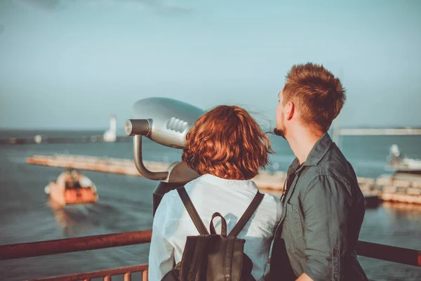 恋爱中的年轻夫妇透过城市双筒望远镜望着海站 在陌生的城市里浪漫地漫步 — 图库照片