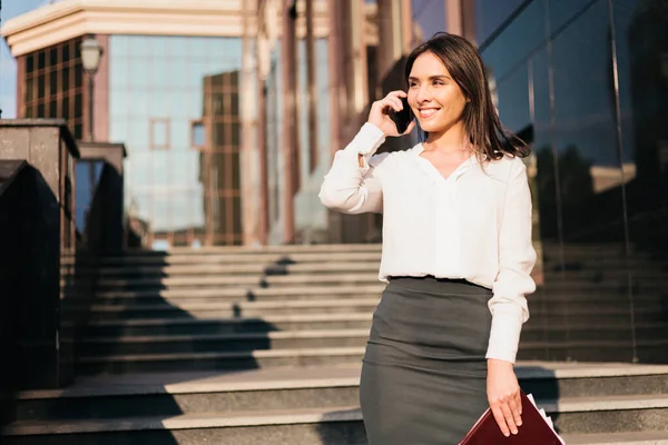 Young attractive business woman in a blouse and a skirt is talking on the phone. Business concept