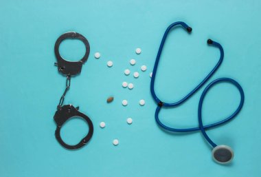 Tıptaki yozlaşma kavramı. Steteskoplu haplar ve mavi arka planda kelepçeler. Tıbbî hayat. Üst görünüm
