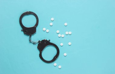 Tıptaki yozlaşma kavramı. Mavi arka planda haplar ve kelepçeler. Tıbbî hayat. Suçun cezası. Üst görünüm