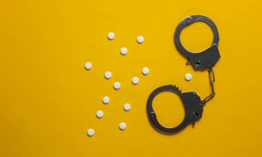 Tıptaki yozlaşma kavramı. Sarı arka planda haplar ve kelepçeler. Tıbbî hayat. Suçun cezası. Üst görünüm