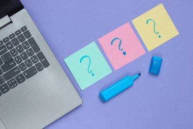 Laptop, üzerinde soru işaretleri ve mor arka planda keçeli kalem olan not kağıtları. Üst görünüm
