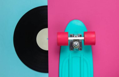Retro tarzı. Plastik mini kruvazör tahtası ve renkli arka planda vinil plak. Pastel renk eğilimi. Yaz eğlencesi. Gençlik minimalist konsepti. 80 'ler. Üst görünüm