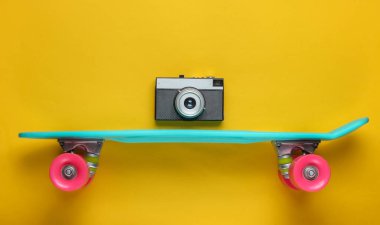 Retro tarzı. Plastik mini kruvazör tahtası ve sarı arka planda retro kamera. Pastel renk eğilimi. Yaz eğlencesi. Gençlik minimalist konsepti. 80 'ler. Üst görünüm