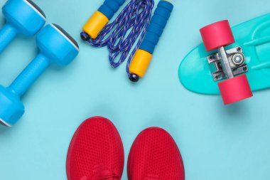 Minimalist spor hala hayatta. Spor kıyafeti. Eğitim için kırmızı spor ayakkabılar ve dambıllar, atlama ipi, mavi arka planda kruvazör tahtası. Yaz eğlencesi. Üst görünüm