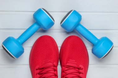 Eğitim için kırmızı spor ayakkabılar, beyaz ahşap zeminde dambıllar. Üst görünüm.