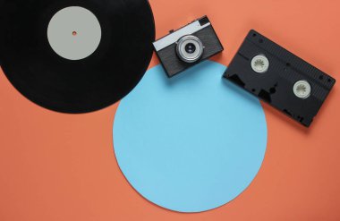 Retro vinil plak, video kaset, mercan rengi arka planda mavi daireli film kamerası. Üst görünüm
