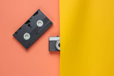 Retro nesneler. Yarı film kamerası, pembe-sarı arka planda video kaset. 80 'ler. Üst görünüm