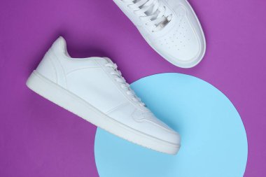 Mor arka planda beyaz spor ayakkabılar ve mavi pastel daire. Gençlik hipster konsepti. Üst görünüm