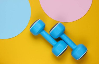 Sarı arka planda plastik halterler ve fotokopi alanı için mavi pastel daireler. Üst Manzara. Minimalist spor konsepti. Üst görünüm