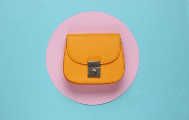 Mavi arka planda sarı renkli deri çanta ve pembe pastel daire. Üst Manzara. Minimalist moda natürmort