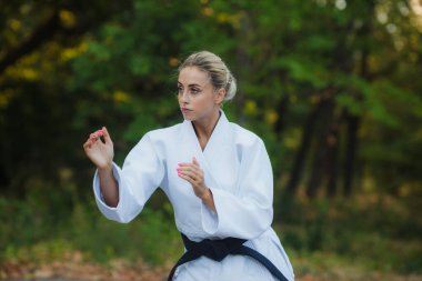 Beyaz kimonolu, siyah kuşaklı çekici kadın dövüşçü açık havada dövüşüyor.