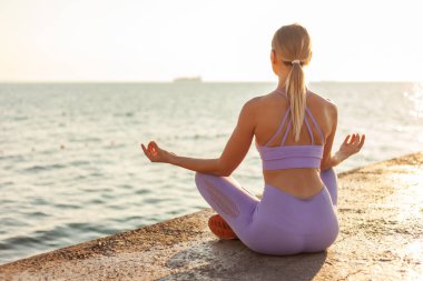 Yoga çalışıyorum. Güneşin doğuşunda meditasyon. Plajda Lotus pozisyonunda oturan sıska genç bir kadın. Sağlıklı yaşam tarzı kavramı