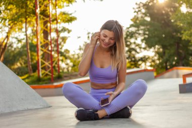 Spor giyim sektöründe genç bir bayan açık havada akıllı telefon kullanıyor. Sağlıklı yaşam tarzı kavramı. Sabah sporu