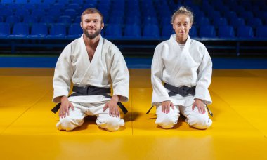 Beyaz kimonolu bir adam ve siyah kemerli bir kadın spor salonunda yere oturup meditasyon yapıyorlar. Doğu dövüş sanatları, judo