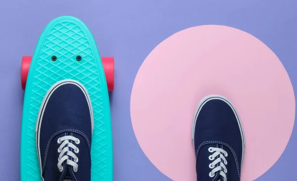 Cruiser board and sneakers on purple background with a pink pastel circle. Youth hipster concept. Summer fun. Top view