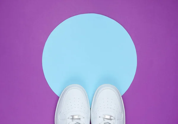 White sneakers on purple background with blue pastel circle for copy space. Youth hipster concept. Top view