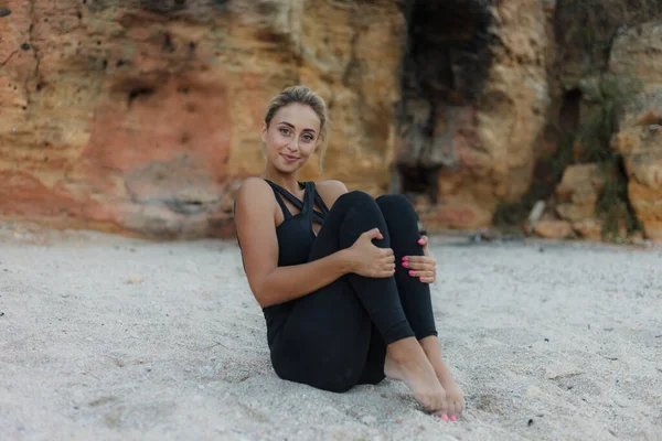 野生のビーチで砂の上に座っている間 スポーツウェアの若い陽気なブロンドの女性の肖像画 健康的なライフスタイルのコンセプト — ストック写真