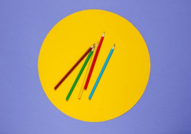 Mor arka planda sarı çemberli renkli kalemler. Stüdyo çekimi