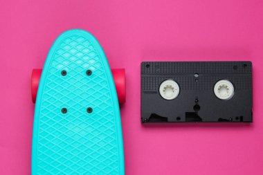 Pop sanatının retro tarzı hala hayat. 80 'ler. Pembe kağıt arka planda kruvazör tahtası ve video kaset. Yaz eğlencesi. Üst görünüm.