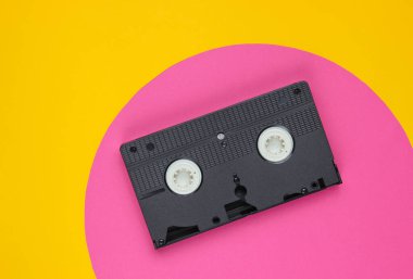 Sarı arkaplanda pembe çemberli video kaset. Stüdyo moda çekimi. 80 'ler, popüler kültür. Üst görünüm.