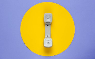 Mor arka planda sarı daireli eski bir telefon ahizesi. Popüler kültür. 80 'ler. Minimalist moda çekimi. Üst görünüm