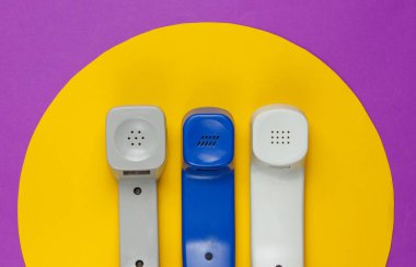 Mor arka planda sarı daireli üç Retro telefon ahizesi. Popüler kültür. 80 'ler. Minimalist moda çekimi. Üst görünüm
