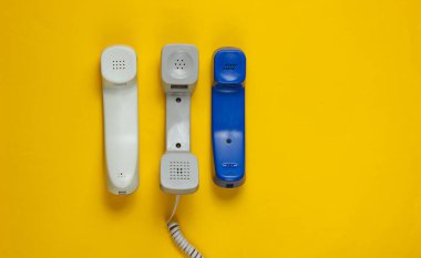 Sarı arkaplanda üç tane ofis telefonu var. Üst görünüm