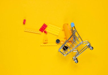 Sarı arka planda oyuncak tuğlaları olan küçük bir alışveriş arabası. Çocuk alışverişi konsepti. Üst görünüm