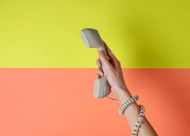 Kabloya sarılı kadın eli renkli arka planda telefon tüpü tutuyor. Liman sanatı. Yaratıcı minimalizm. Üst görünüm