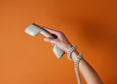 Kabloya sarılmış bir kadın telefon tüpünü kahverengi arka planda tutuyor. Liman sanatı. Yaratıcı minimalizm. Üst görünüm