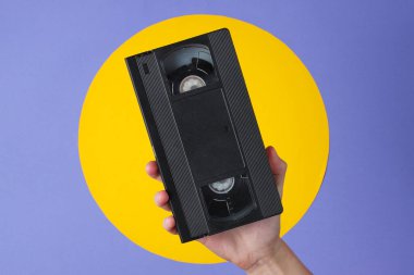 Mor zemin üzerinde sarı çemberli video kaset tutan kadın.