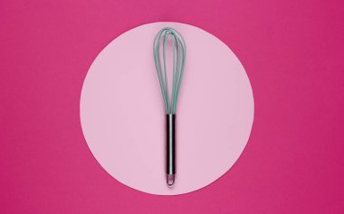 Ortasında pastel renk çemberi olan pembe arka planda bir mutfak çırpısı. Üst Manzara. Minimalizm