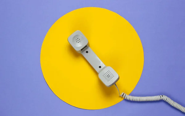 Retro telephone handset on a purple background with a yellow circle. Pop culture. 80s. Minimalistic fashion shot. Top view