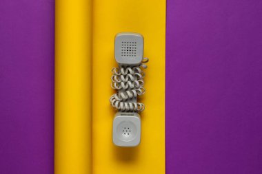 Mor-sarı arka planda, eski telefon ahizesi sarmalanmış kablo. Minimalizm modadır. Üst görünüm