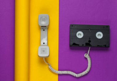 Telefon ahizesi ve sarılıp sarmalanmış mor kağıt arka planda video kaset. Renkli trend, minimalist moda natürmort hayat. Üst görünüm