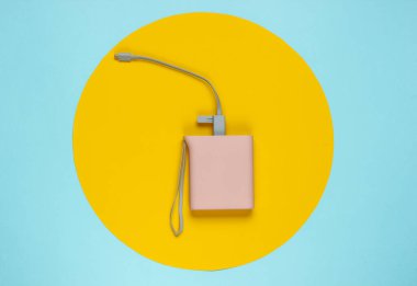 Güç bankası mavi arkaplanda, ortasında sarı halka var. Pastel renk eğilimi, minimalist durgun yaşam. Modern aletler. Üst görünüm