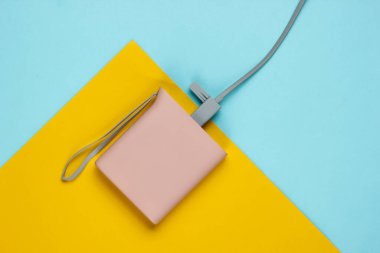 Güç bankası mavi sarı kağıttan arka planda. Pastel renk eğilimi, minimalist durgun yaşam. Modern aletler. Üst görünüm