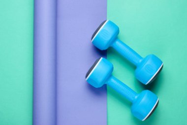 Ambalajlı kağıdın üzerinde mavi plastik halterler. Renk trendi, minimalist spor ve moda natürmort. Üst görünüm