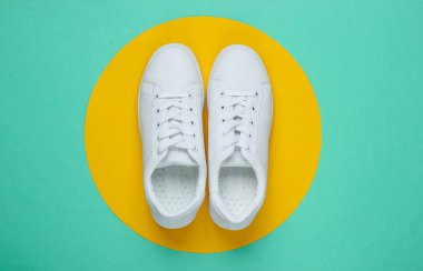 Mavi kağıttan arka planda sarı daireli şık beyaz ayakkabılar. Minimalist moda konsepti. Üst görünüm