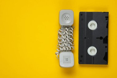 Modası geçmiş bir cep telefonu, sarı arka planda video kaset. Üst görünüm