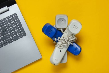 Laptop ve sarı arka planda kabloyla sarılı bir sürü cep telefonu. Minimalist ofis konsepti, çağrı merkezi. Üst görünüm
