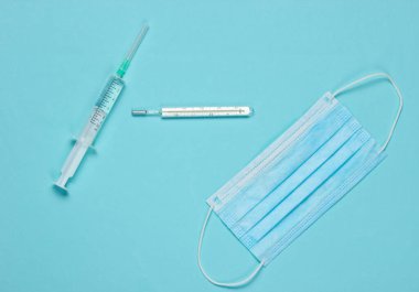 Mavi arka planda tıbbi hayat. Şırınga, tıbbi maske, termometre. Minimalizm